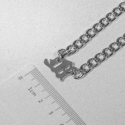Silver Gothic letter pendant on a sturdy unisex chain necklace next to a ruler for size reference.