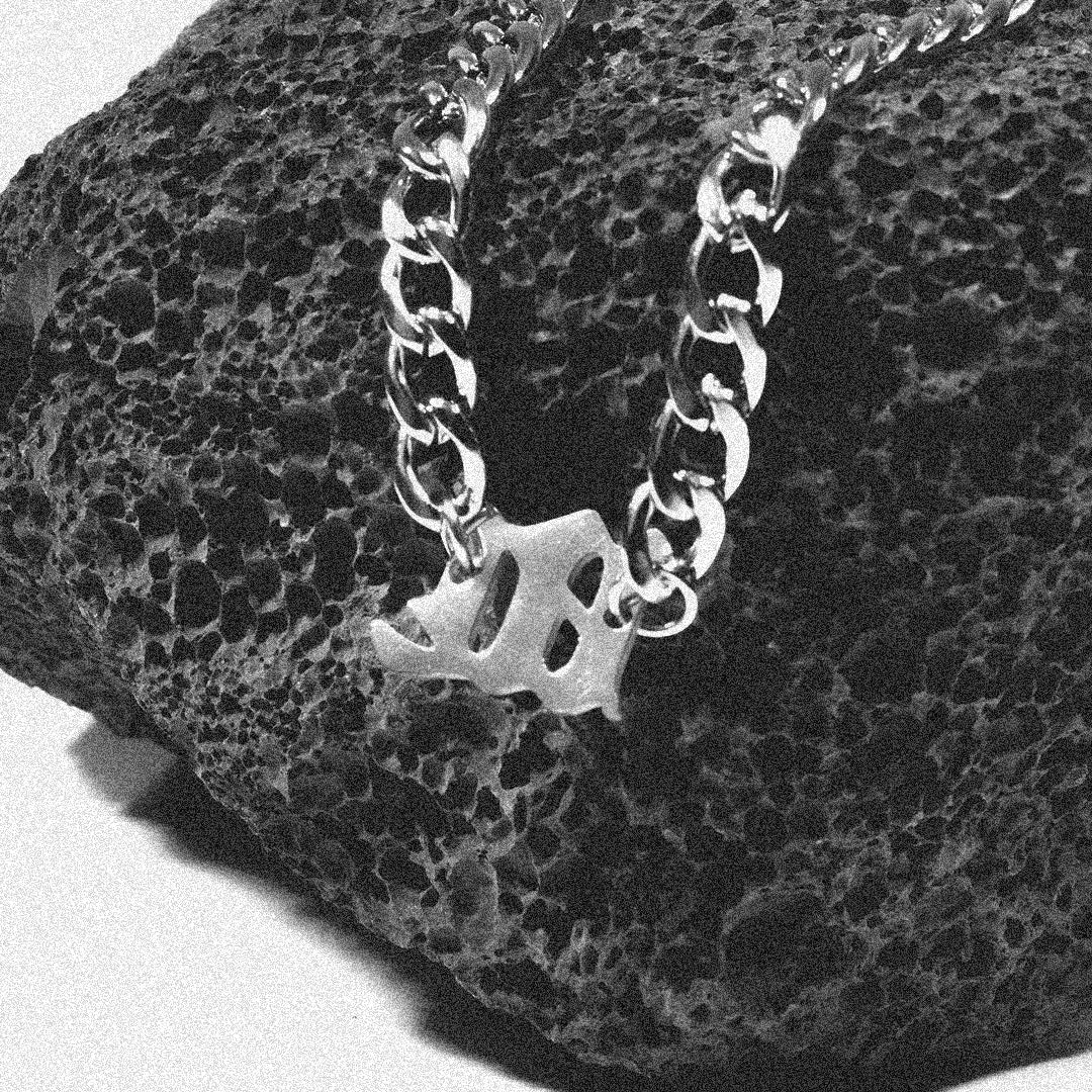 Unique Gothic letter pendant on a silver unisex chain necklace displayed on a textured black stone.