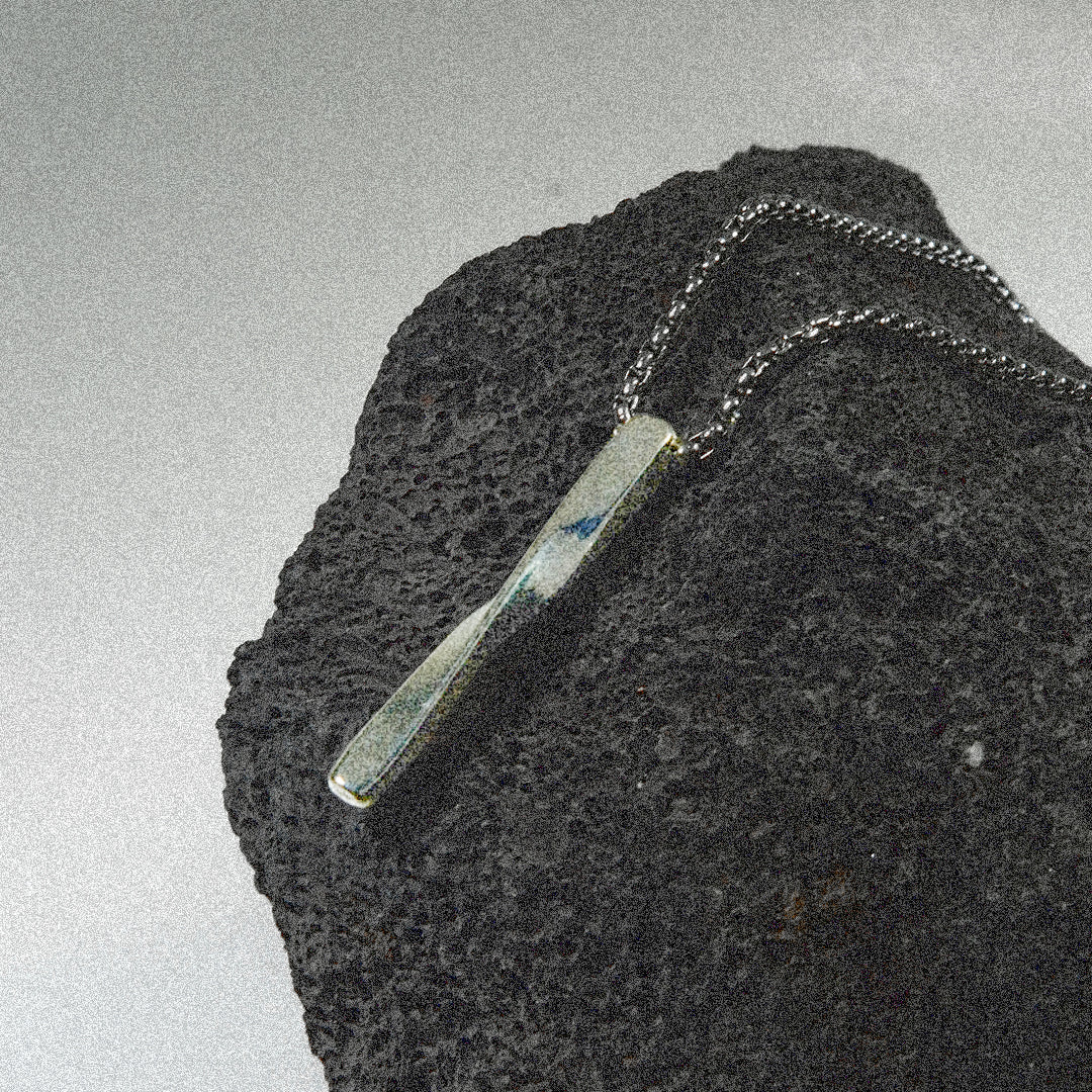 A sleek black rock adorned with a shiny silver bar necklace resting on top.