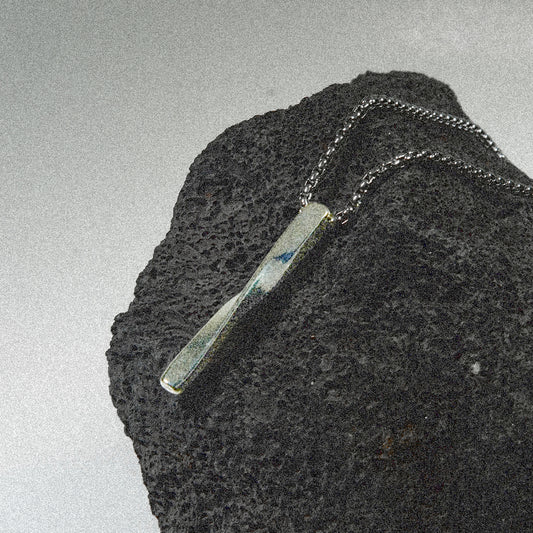 A sleek black rock adorned with a shiny silver bar necklace resting on top.