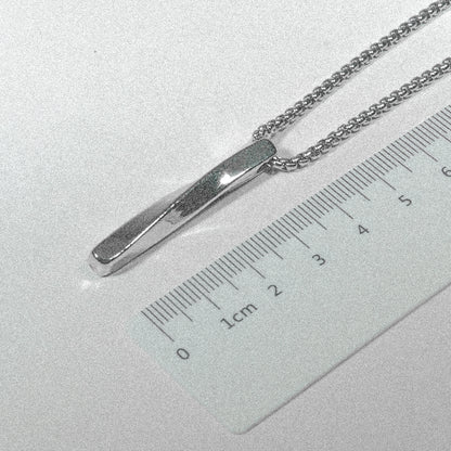 A silver necklace with a ruler resting on top, showcasing a unique blend of elegance and practicality.